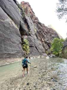 Katie hiking through the Zion Narrows, wading through the river with trekking poles